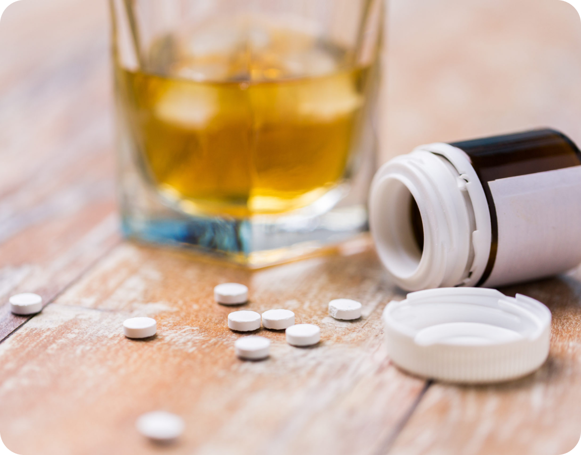 Glass of alcohol with box of pills opened and spilled on the table